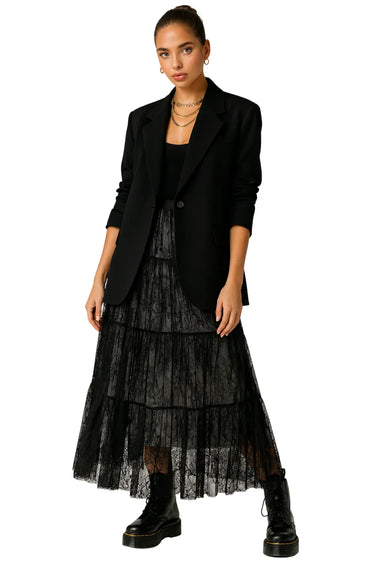 Woman wearing a black blazer, black top, and black lace maxi skirt on a white background